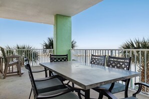 An outdoor patio with a table and chairs, surrounded by a railing, palm trees, and a clear sky. - Hooked Bliss|Bay Views+Boat Slip+Beach Access (Gulf Shores)