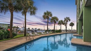 A swimming pool with lounge chairs, palm trees, and a building in the background. - Hooked Bliss|Bay Views+Boat Slip+Beach Access (Gulf Shores)