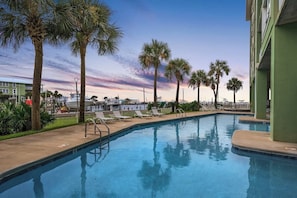 A swimming pool with lounge chairs, palm trees, and a building in the background. - Hooked Bliss|Bay Views+Boat Slip+Beach Access (Gulf Shores)