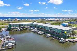 Un port de plaisance avec des bateaux amarrés, un grand bâtiment à la façade verdoyante et, au loin, une vue dégagée sur l’océan.