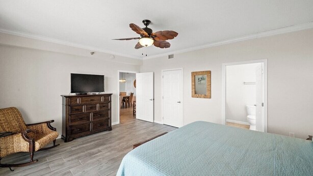 A bedroom with a bed, a dresser, a television, a ceiling fan, and a door leading to a bathroom. - Hooked Bliss|Bay Views+Boat Slip+Beach Access (Gulf Shores)