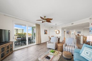 A spacious living room with a large flat-screen TV, a ceiling fan, and a balcony with outdoor furniture. - Snowbird Rates Hooked Bliss Bay Views Boat Slip (Gulf Shores)