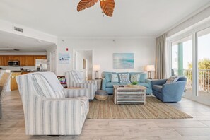Un salon moderne avec des canapés à rayures, une table basse et une vue sur l’océan grâce à de grandes fenêtres.
