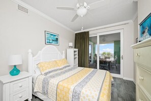 A bedroom with a bed, a nightstand, a dresser, a ceiling fan, a window with curtains, and a view of an outdoor patio. - Snowbird Rates Hooked Bliss Bay Views Boat Slip (Gulf Shores)