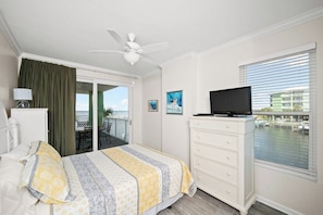 Une chambre d’hôtel avec un lit, un téléviseur posé sur une commode, un balcon avec vue et un ventilateur de plafond.