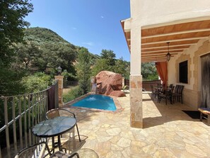 Ein Poolbereich mit Steinboden, einem Tisch mit Stühlen und Blick auf eine Berglandschaft.