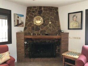 Ein Wohnzimmer mit Kamin aus Stein, einem Schachbrett und einem gerahmten Porträt an der Wand.