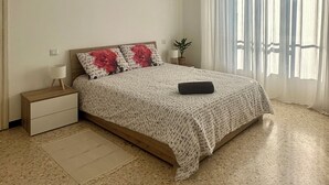 A bedroom with a bed, a nightstand, a ceiling fan, a window with sheer curtains, and a potted plant. - Moelda Home | Milan-Malpensa MXP 15′ Milan-Fiera (legnano)