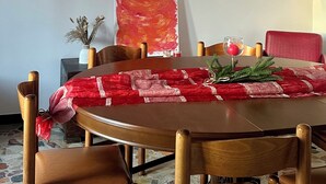 A dining area with a round table, wooden chairs, a red tablecloth, a red chair, a vase with dried flowers, and a large abstract painting on the wall. - Moelda Home | Milan-Malpensa MXP 15′ Milan-Fiera (legnano)