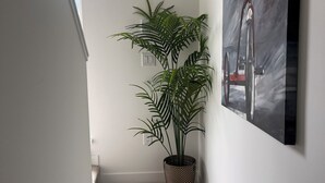 Een gang met een kamerplant en een schilderij aan de muur.