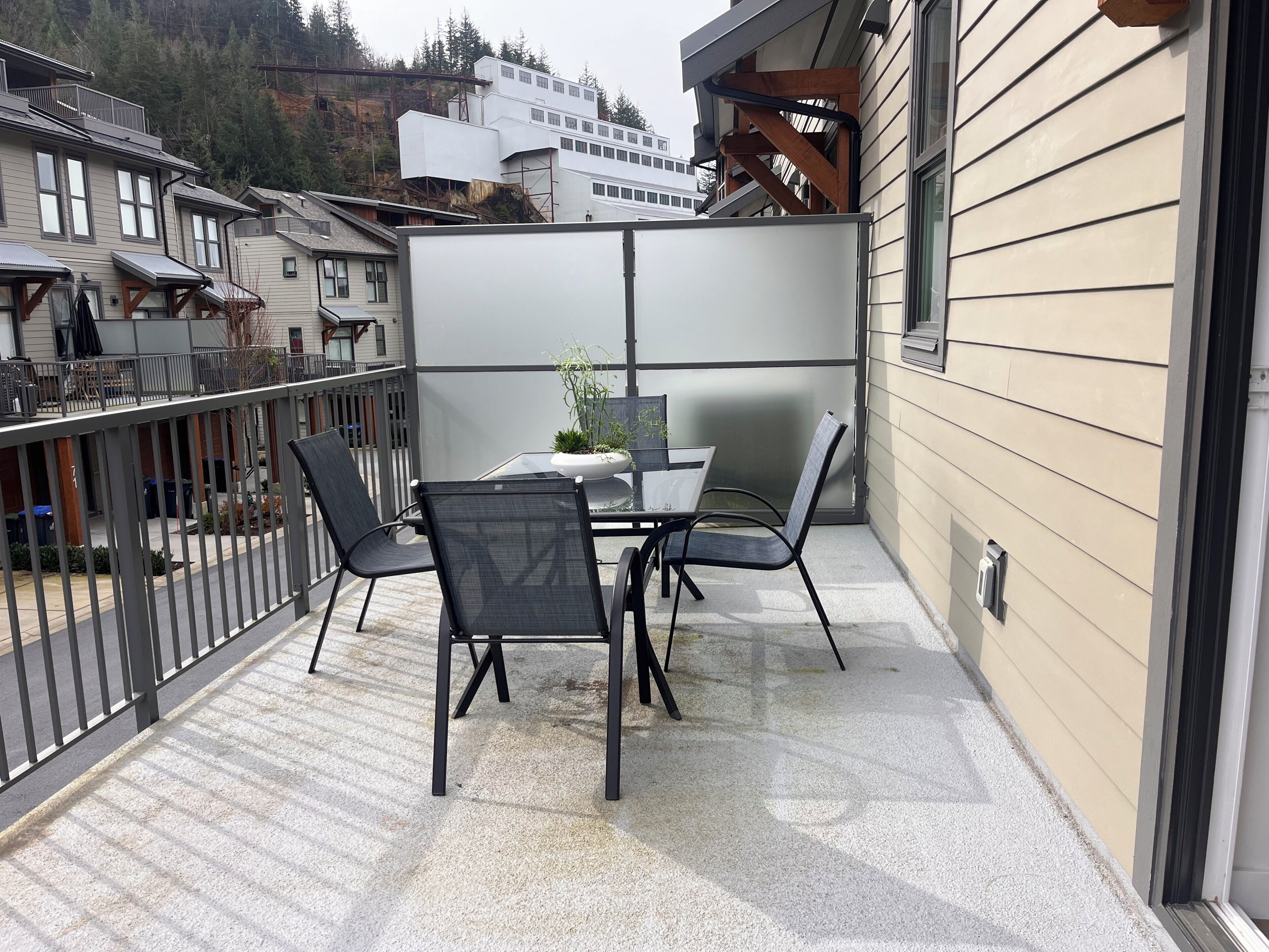 A balcony with a table and chairs, a potted plant, and a view of a forested hillside.