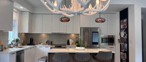 Una cocina moderna con una isla central, electrodomésticos de acero inoxidable y una lámpara original con forma de asta de ciervo.