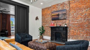 A modern living room with a brick wall, a fireplace, and a cityscape painting. - The Stables | Walkable, MiniGolf, Fire Pits, Games (Louisville)