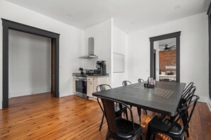 Eine moderne Küche mit Edelstahlgeräten, ein Essbereich mit einem dunklen Holztisch und schwarzen Stühlen sowie eine Ziegelwand im Hintergrund.