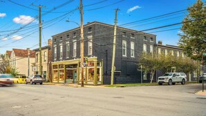A two-story building with a storefront on the ground floor, a clear sky, and parked cars on the street. - The Stables | Walkable, MiniGolf, Fire Pits, Games (Louisville)