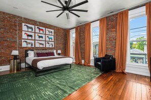 Ein Schlafzimmer mit Ziegelwand, einem Bett, einem grünen Teppich, einem schwarzen Lederstuhl und einem Deckenventilator.