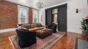 A spacious living room with a leather sofa, a dark armchair, a tufted ottoman, and a patterned rug. - The Stables | Walkable, MiniGolf, Fire Pits, Games (Louisville)