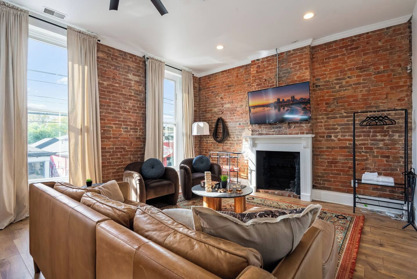 Una sala de estar con pared de ladrillo, sofá de cuero, sillones, chimenea y televisor.