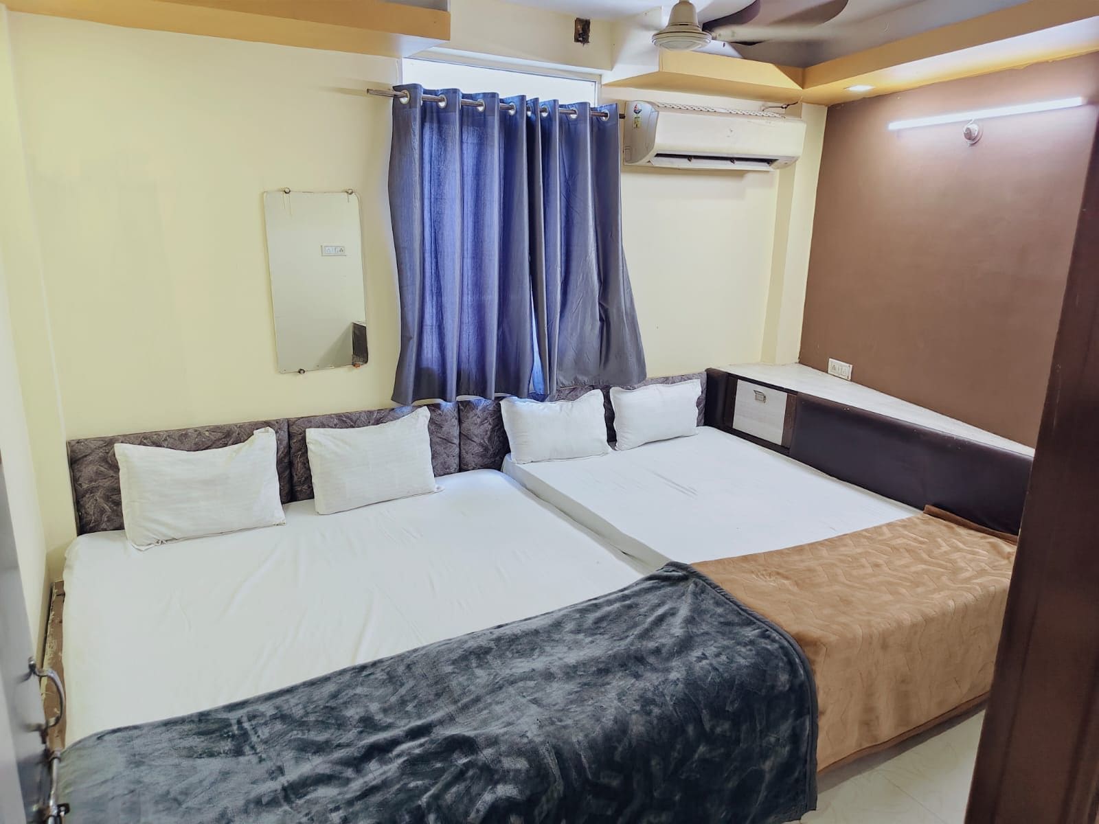 Habitación de hotel con dos camas, ventilador de techo, aire acondicionado y ventana con cortinas.