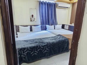 Una cama doble con una colcha estampada oscura, una mesita de noche y un equipo de aire acondicionado de pared.