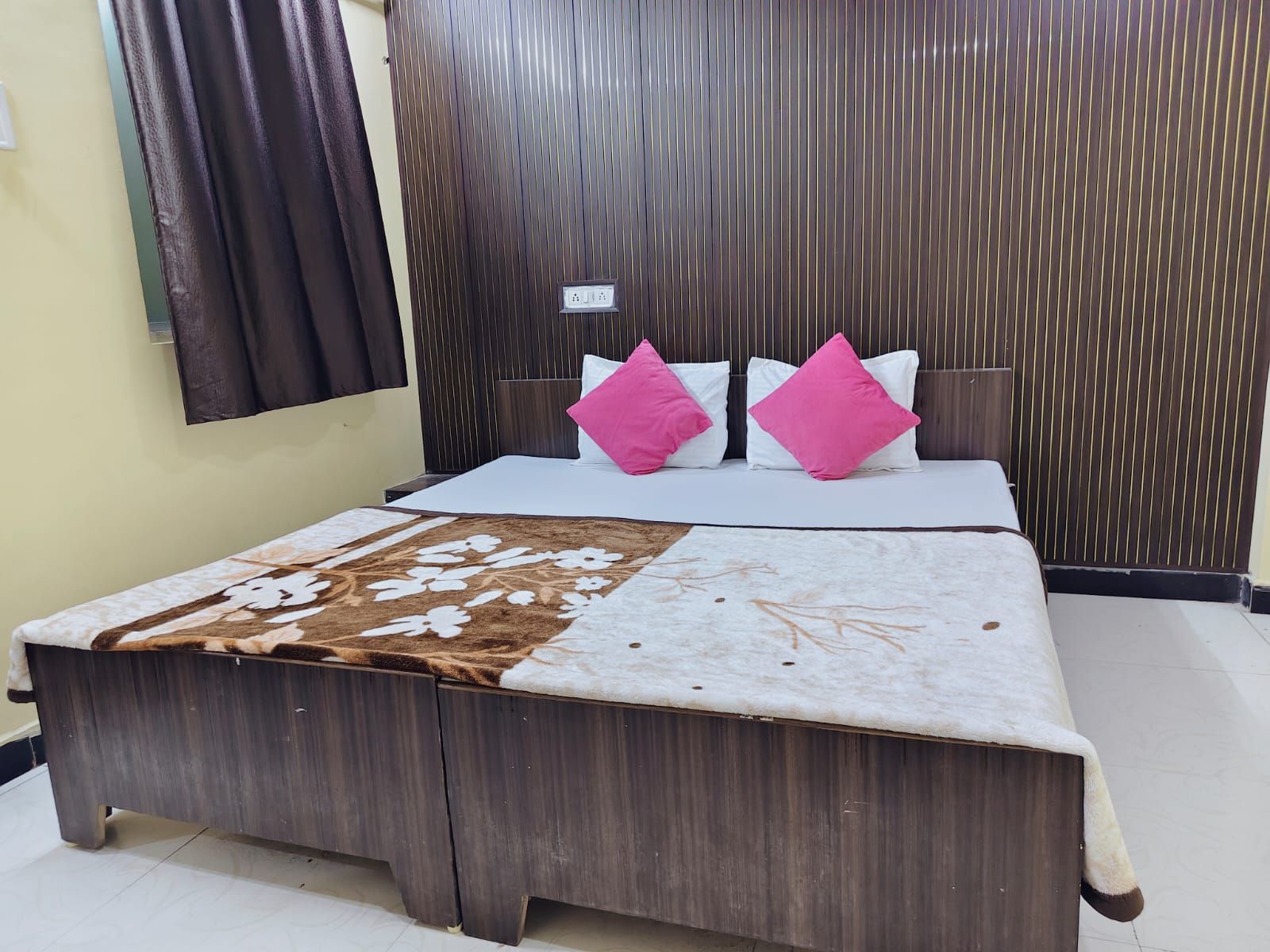 A bedroom with a wooden bed, two pillows, a patterned bedspread, and a dark curtain.