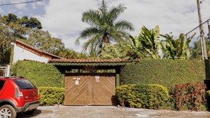 En grind med en träport, en röd bil parkerad framför, och frodig grönska med bland annat palmer och bananplantor.