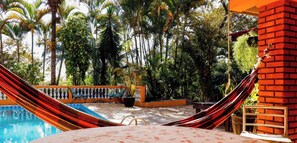 A pool area with a hammock, palm trees, and a brick wall. - Sitio em Itupeva com Piscina e Churrasqueira (Itupeva)