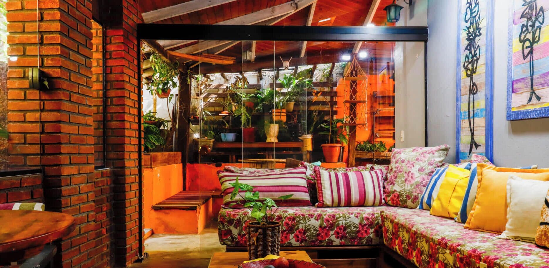 A cozy living room with a brick wall, a sofa with floral upholstery, and various potted plants.