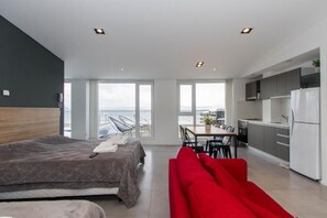 A modern hotel room with a bed, a red sofa, a dining area, and a kitchen. - Costa Apartamentos (Ushuaia)