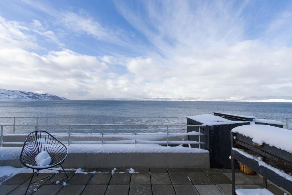 En snedækket terrasse med en stol og en bænk, med udsigt over vand og fjerne bjerge.