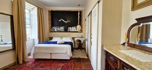 A hotel room with a bed, a mirror, a chandelier, and a red patterned rug. - COPEL0100 - Prédio 34 (Salvador)