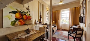 A hotel room with a dining area, a painting of fruit on the wall, a chandelier, and a view of the outside. - COPEL0100 - Prédio 34 (Salvador)