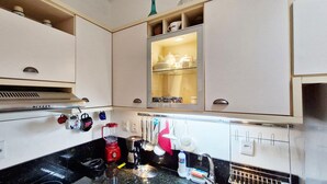 A kitchen with white cabinets, a stainless steel range hood, and various kitchen utensils hanging on the wall. - COPEL0100 - Prédio 34 (Salvador)