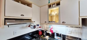 A kitchen with white cabinets, a stainless steel range hood, and various kitchen utensils hanging on the wall. - COPEL0100 - Prédio 34 (Salvador)