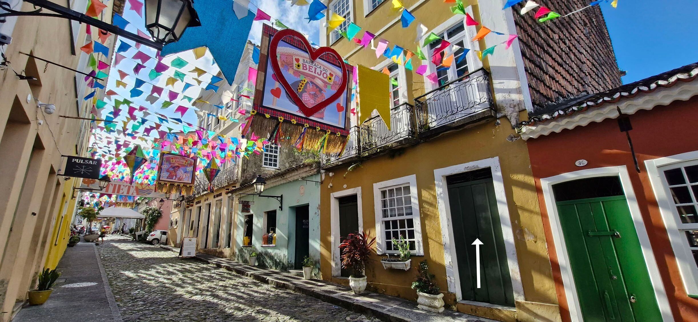 A narrow street with colorful flags and a heart-shaped sign.