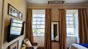 A hotel room with a bed, a television mounted on the wall, a window with curtains, and a view of the outside. - COPEL0100 - Prédio 34 (Salvador)