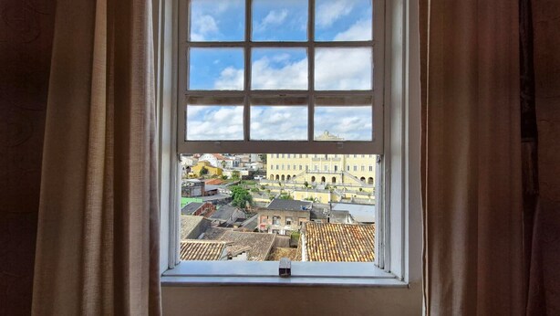 A window with a view of a cityscape, curtains, and a clear sky. - COPEL0100 - Prédio 34 (Salvador)