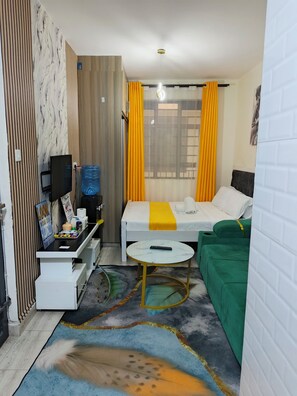 A compact hotel room with a bed, a small table, a TV, and a water dispenser. - Adorable 1-bedroom apartment in Nairobi 20 mins drive from JKIA welcome (Nairobi)