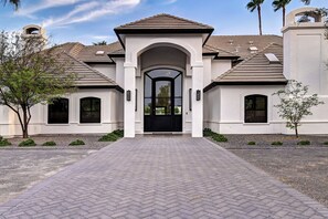 Une maison à deux étages, dotée d’une façade symétrique, d’une entrée centrale avec une porte noire et d’une allée pavée avec un motif en chevrons.