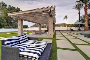Ein Patio-Bereich mit einer Pergola, Gartenmöbeln und einem Schwimmbecken.