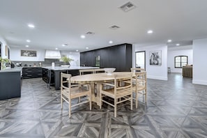 Eine moderne Küche mit einer zentralen Kochinsel, dunklen Schränken und einem Essbereich mit Holztisch und Stühlen.