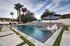 Une piscine bordée de pierres, entourée d’un patio aménagé avec des chaises et des parasols.
