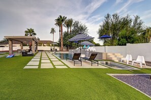 Ein Garten mit Pool, Liegestühlen und einer Pergola.