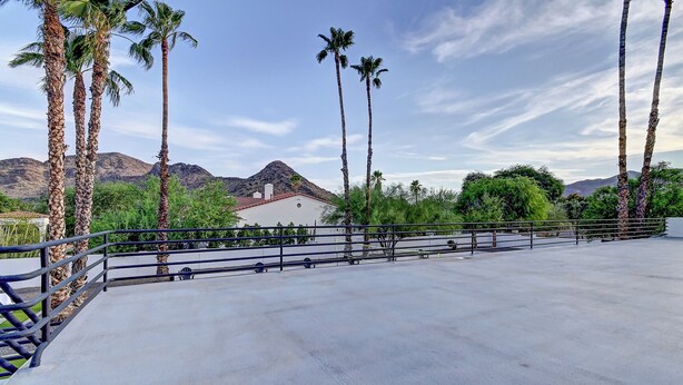 Eine Terrasse im Freien mit Betonboden, umgeben von Palmen und einem Berg im Hintergrund.