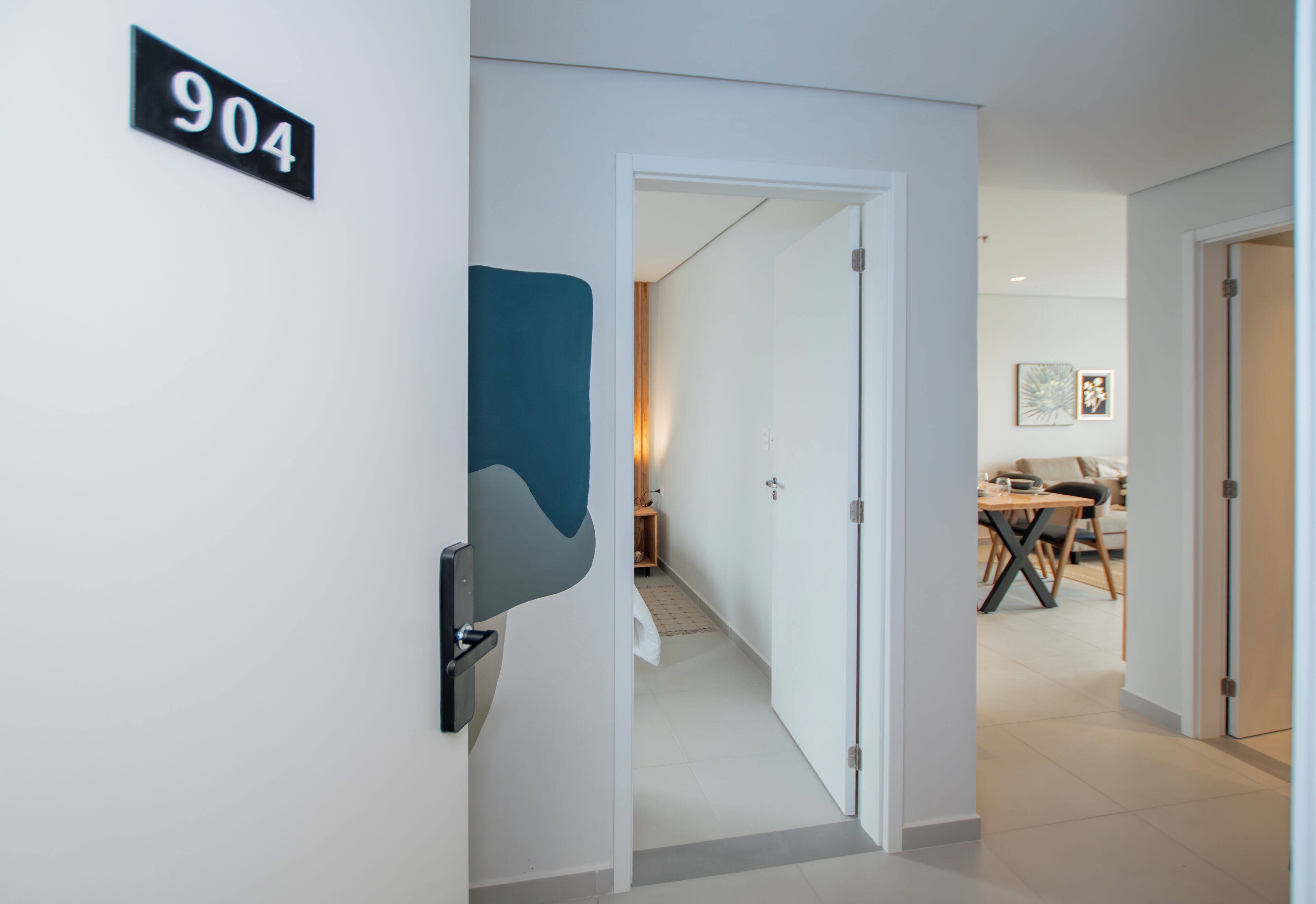 A hallway with a door leading to a dining area, a number sign '904', and a modern abstract wall art piece.
