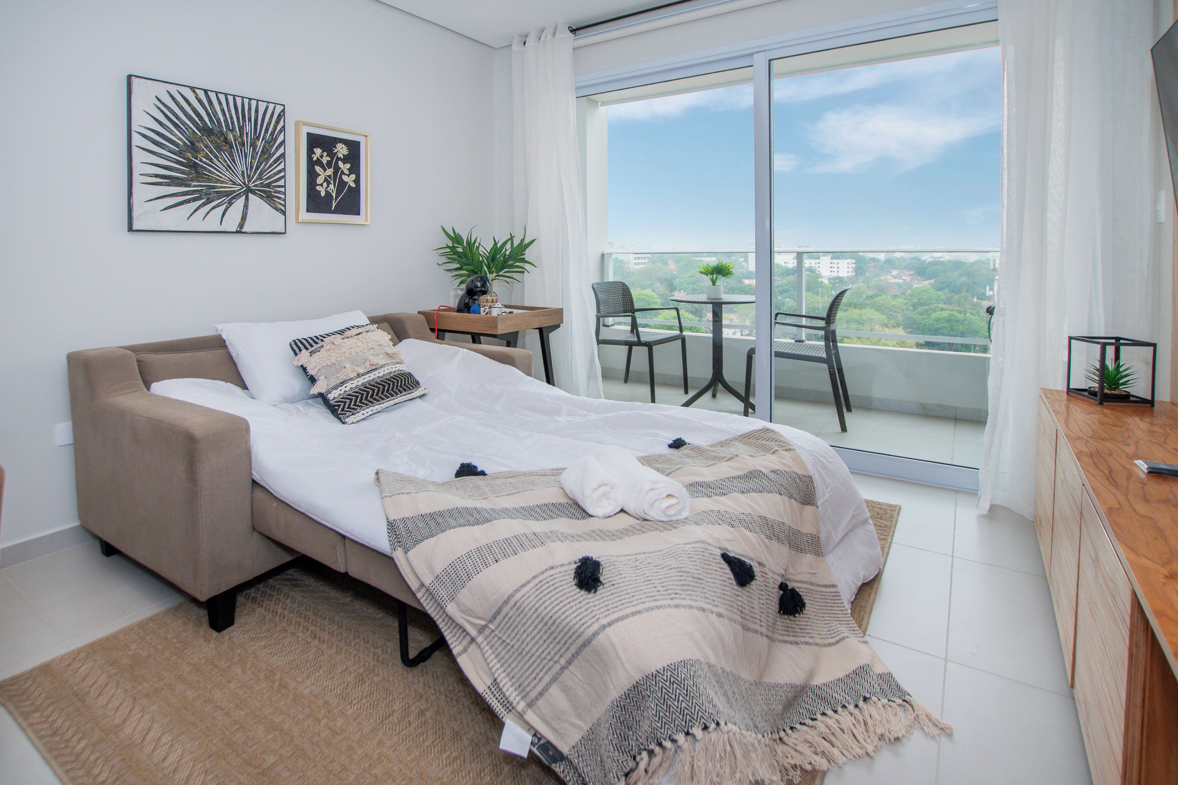 Ein modernes Schlafzimmer mit einem Bett, einem kleinen Tisch mit Pflanze und einem Balkon mit Stühlen.