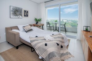 A modern bedroom with a bed, a small table with a plant, and a balcony with chairs. - Corporate Stays First Living - 904 (Asunción)