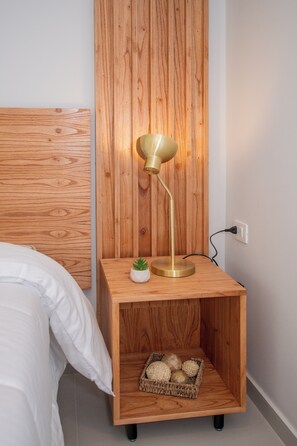 A wooden bedside table with a lamp, a small potted plant, and a basket of decorative items. - Corporate Stays First Living - 904 (Asunción)