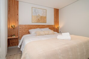 Ein ordentlich bezogenes Bett mit Kopfteil, ein Nachttisch mit Lampe und ein an der Wand hängendes Kunstwerk.
