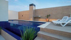 Ein Swimmingpool mit klarem, blauen Rand, ein moderner Außenbereich mit Liegestühlen und ein Blumentopf.